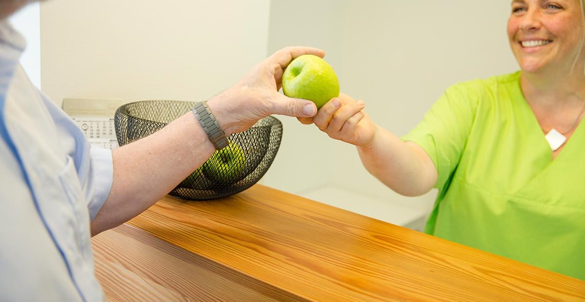 Mitarbeiterin Bernadette Mendel gibt Patienten einen knackigen grünen Apfel