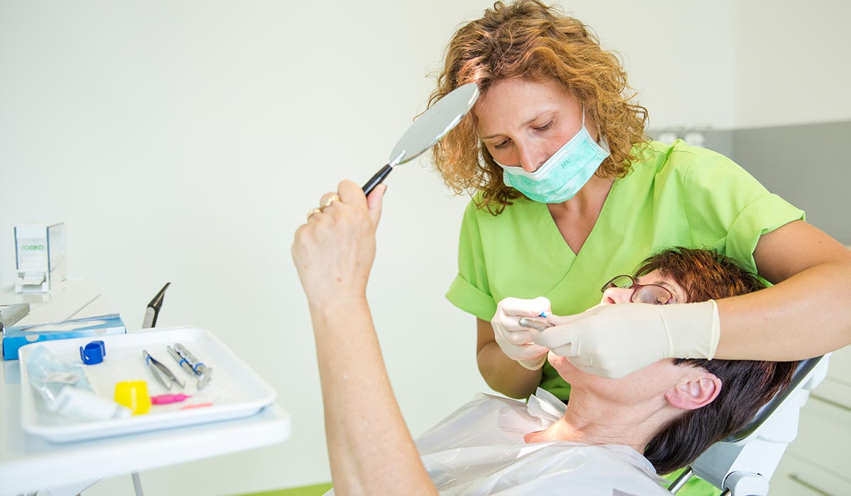 Patientin im Zahnarztstuhl beobachtet die Arbeiten der Mitarbeiterin im Spiegel, während sie eine Füllung gesetzt bekommt.
