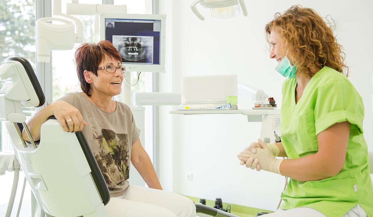 Mitarbeiterin Cornelia Renneberg lächelt Patienten im Behandlungsstuhl an, die zurücklächelt