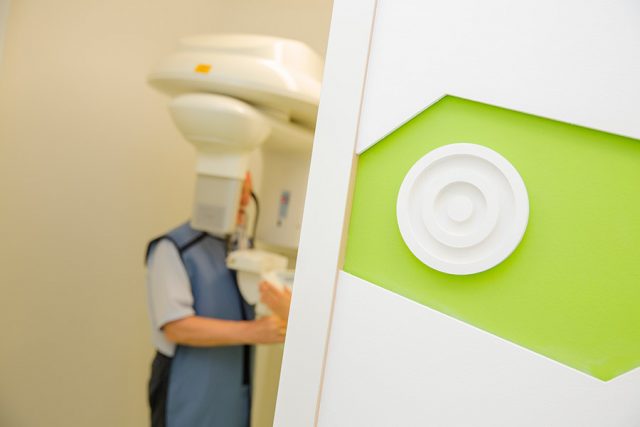 Rechts ist eine Wand zu sehen, links sieht man einen Patienten, der in einem 3D-Röntgengerät steht.