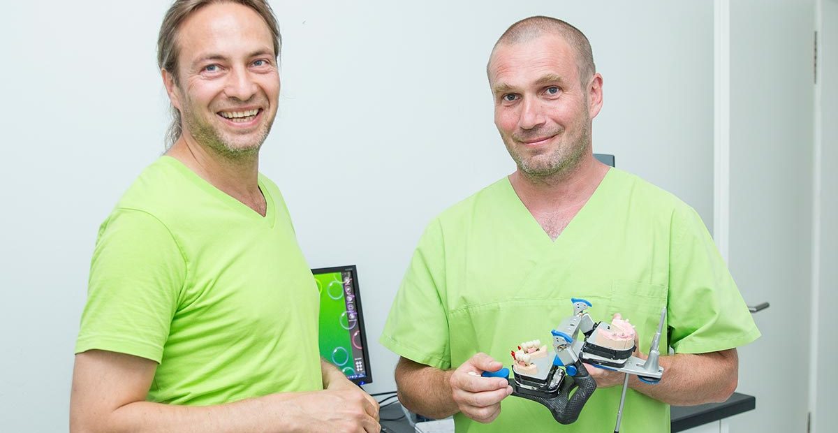 Zahntechniker Thomas Beinroth und Zahnarzt Dr. Dr. Thomas Buchmann, der ein Modell für Zahnersatz in den Händen hält.