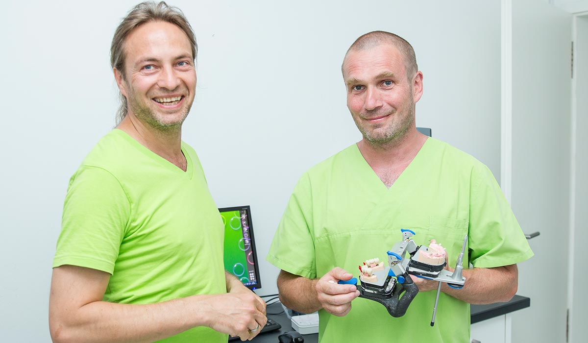 Zahntechniker Thomas Beinroth und Zahnarzt Dr. Dr. Thomas Buchmann, der ein Modell für Zahnersatz in den Händen hält.